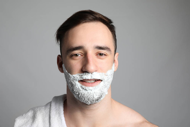 Hombre guapo con espuma de afeitar en su cara contra fondo gris
 - Foto, imagen