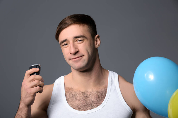 Bonito homem com barbeador elétrico e balões de ar no fundo cinza
 - Foto, Imagem