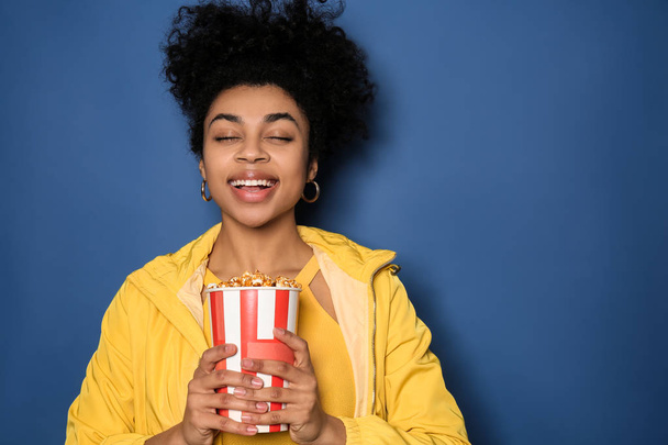 Portrait of young African-American woman with popcorn  on color background - Foto, Imagem