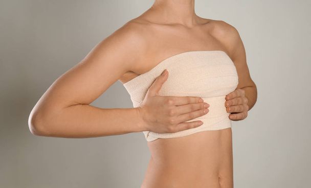 Frau mit Verband auf der Brust vor grauem Hintergrund. Konzept zur Brustvergrößerung - Foto, Bild