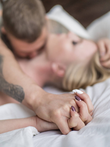 Adult couple lying on the bed in the hotel. the man leaned over young woman, his hands holding her arm. Focus on hands. Love and relationships concept - Photo, Image