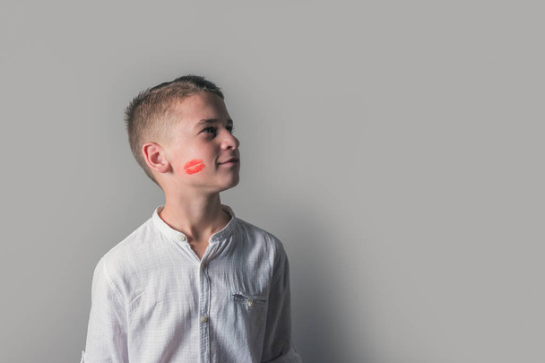 Cute boy with lipstick kiss on his face on bright background. - Фото, изображение