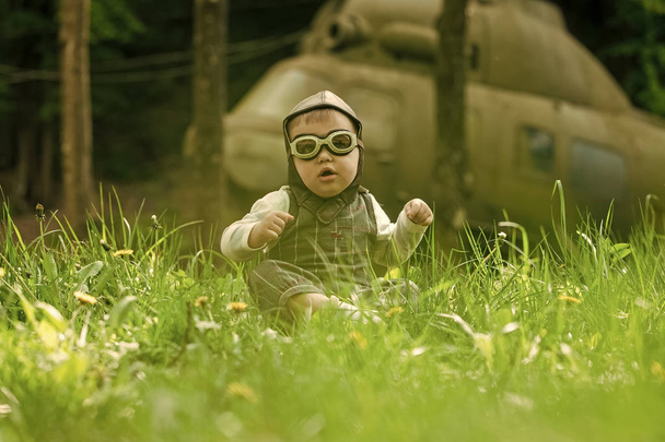 Boy in pilot helmet and glasses sitting in green grass - Valokuva, kuva