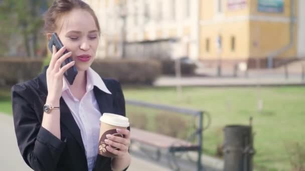 Şehir merkezinde, kahve içme iş ortağı ile konuşurken profesyonel kadın işveren akıllı telefon kullanan genç başarılı işkadını. İş bölgesi gökdelenler arka planda - Video, Çekim