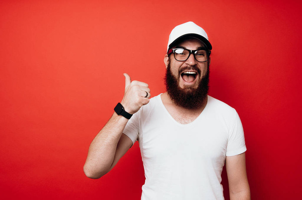 Cheerful excited bearded man showing thumbs up over red wall - Foto, immagini