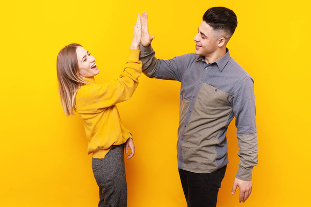 Portrait of happy smiling couple giving high five to each over over yellow background - Photo, Image