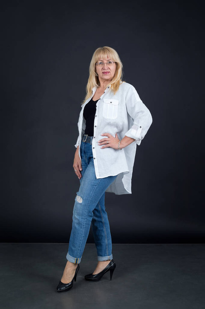 Portrait of a full length adult woman in jeans and white shirt on a dark background. - Photo, Image