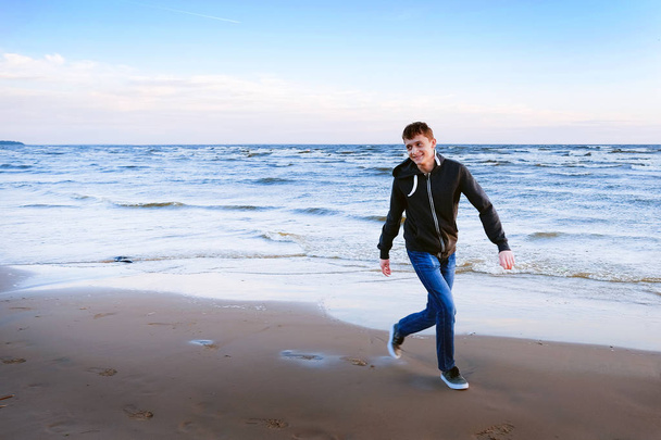 Free happy young man standing on the beach with his arms outstretched like a bird, feeling the warm wind looking into the distance, relaxed and carefree. - Photo, image