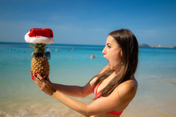meisje op het strand in een New Year's hoed in afwachting van het nieuwe jaar en kerst met ananas - Foto, afbeelding