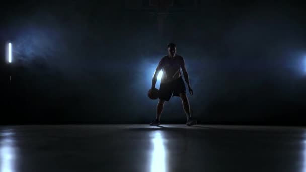 Мастерство дриблинга баскетболиста в темноте на баскетбольной площадке с подсветкой назад в дыму. Медленное движение стритбола
. - Кадры, видео