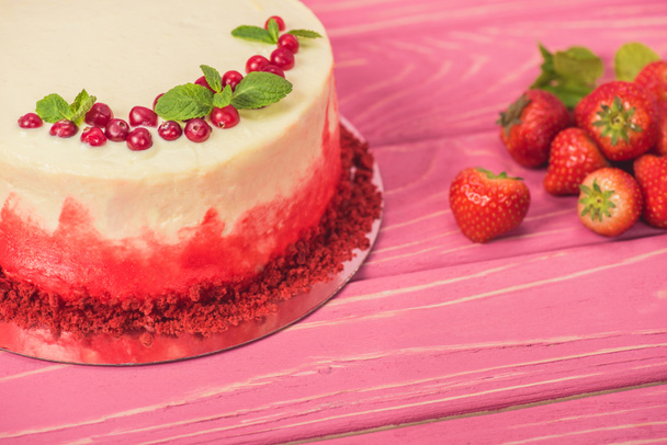 close up of white cake decorated with red currants and mint leaves near strawberries - Фото, изображение