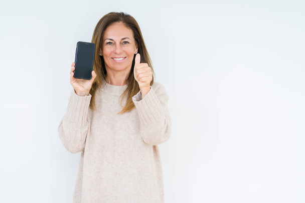 A középkorú nő bemutatás képernyő smartphone elszigetelt háttérhez képest boldog ezzel rendben van a jel, hüvelykujjával felfelé ujjaival, kiváló jel nagy mosollyal - Fotó, kép