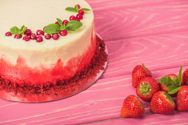 close up white cake decorated with currants and mint leaves near red strawberries - Foto, Imagen