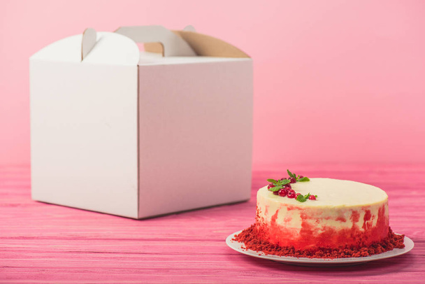 pastel decorado con grosellas y hojas de menta cerca de paquete blanco aislado en rosa
 - Foto, imagen