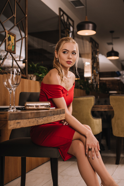 aantrekkelijke vriendin in rode jurk zittend in restaurant en wachten van vriendje - Foto, afbeelding