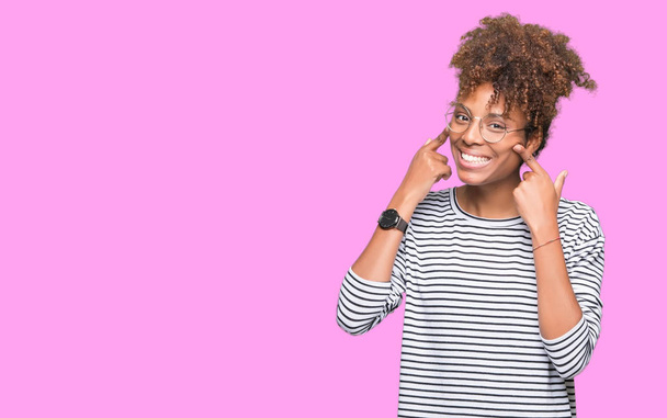 Mooie jonge african american vrouw dragen bril over geïsoleerde achtergrond Smiling met open mond, vingers wijzen en dwingen vrolijke glimlach - Foto, afbeelding