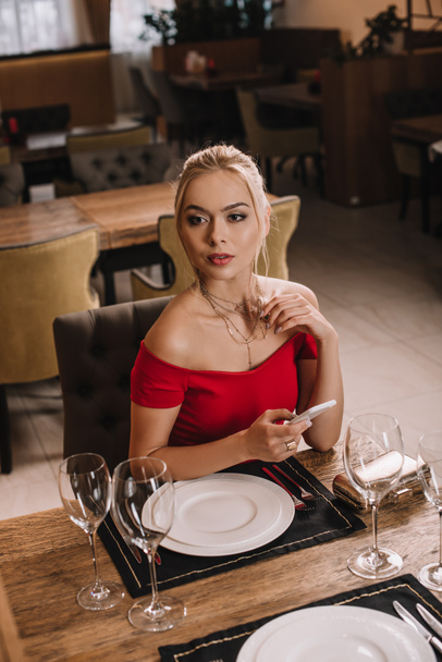 atractiva novia en vestido rojo sentado en el restaurante y esperando novio
 - Foto, Imagen