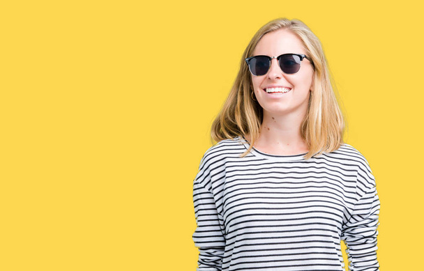 Mooie jonge vrouw dragen van een zonnebril op geïsoleerde achtergrond op zoek weg aan kant met glimlach op het gezicht, natuurlijke wijze van uitdrukking. Lachen vertrouwen. - Foto, afbeelding