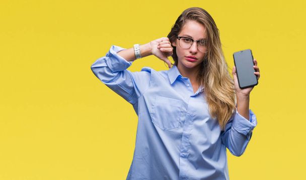 Mladá krásná blondýna obchodních žena zobrazeno obrazovka smartphone izolované pozadí s naštvaný obličej, záporné znaménko ukazující nechuť s palci dolů, koncept odmítnutí - Fotografie, Obrázek