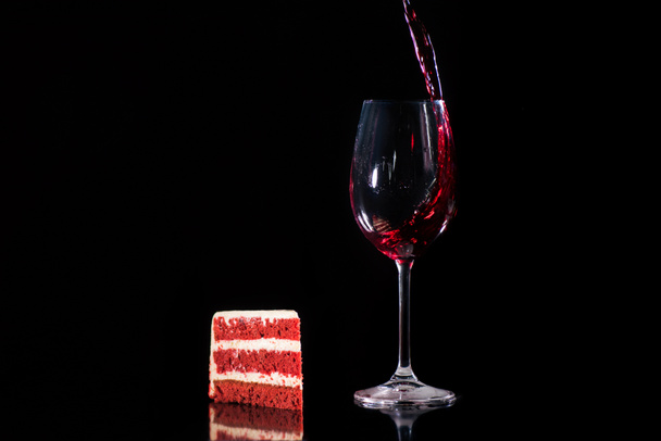 piece cake near glass of red wine isolated on black - Foto, Imagem