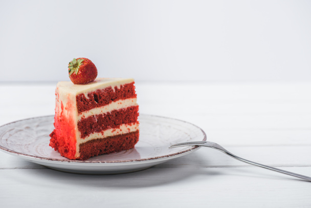piece of red cake decorated with strawberry on saucer isolated on white  - Foto, afbeelding