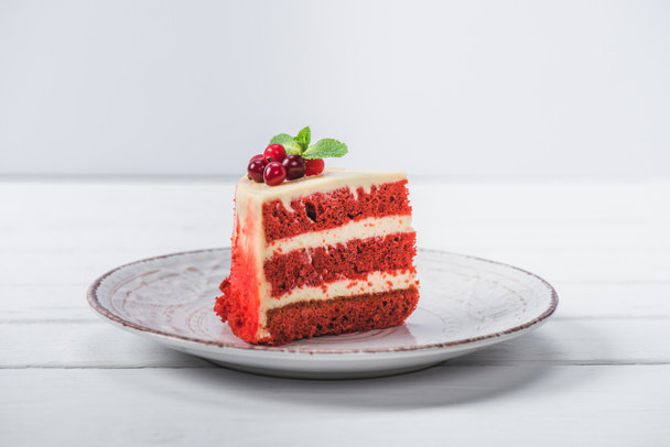 κομμάτι κόκκινο κέικ διακοσμημένο με σταφίδες σε πιατάκι που απομονώνονται σε λευκό  - Φωτογραφία, εικόνα