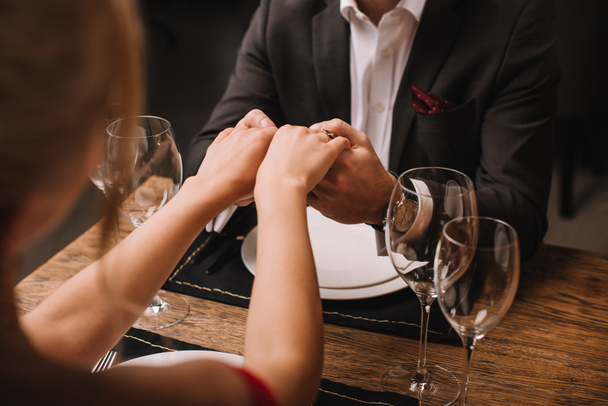 boyfriend in suit and girlfriend holding hands in restaurant - Foto, Imagen