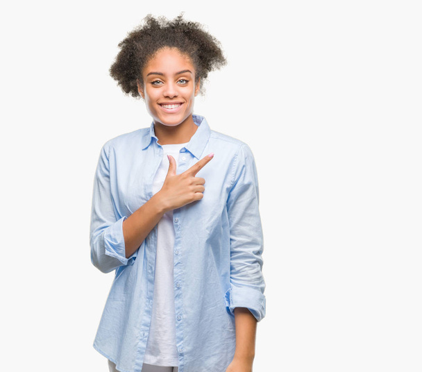 Молодая афро-американская женщина на изолированном фоне веселый с улыбкой лица указывая рукой и пальцем в сторону со счастливым и естественным выражением лица, глядя в камеру
. - Фото, изображение