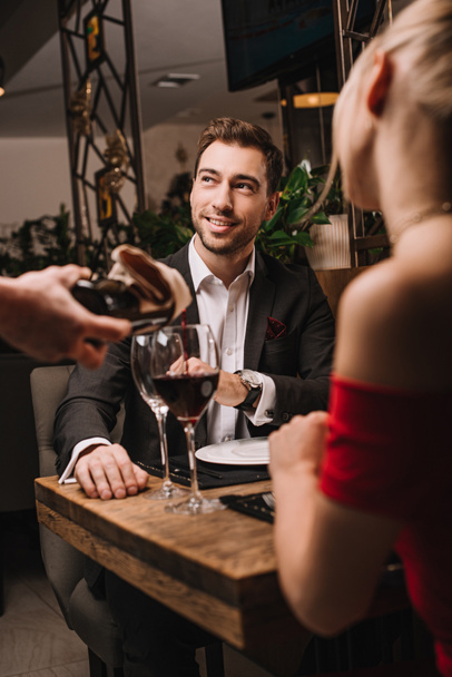 Selektivní fokus pohledný muž dívá na číšník nalil do sklenice červené víno  - Fotografie, Obrázek