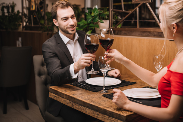 cheerful man toasting with red wine and smiling to girlfriend in restaurant  - 写真・画像