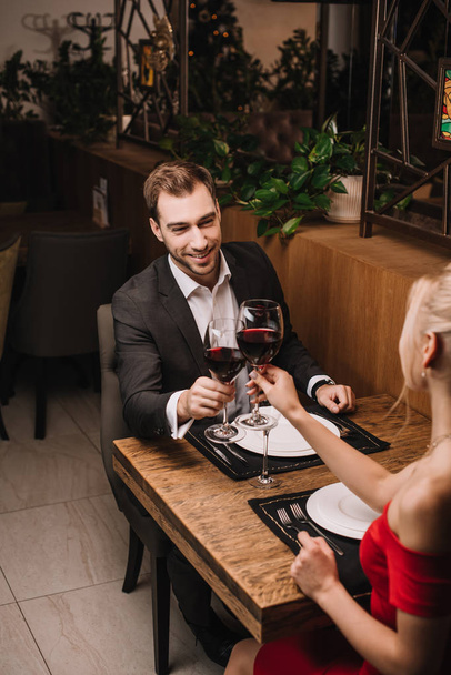 happy man toasting with wine and smiling to girlfriend in restaurant  - Zdjęcie, obraz