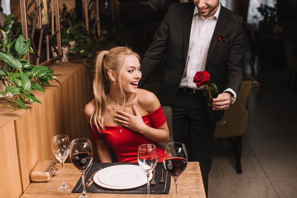 ο φίλος που δίνει κόκκινο τριαντάφυλλο έκπληκτος φίλη στο εστιατόριο  - Φωτογραφία, εικόνα