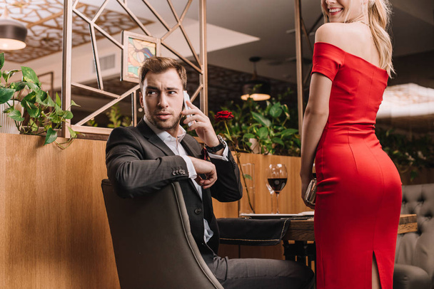 handsome man talking on smartphone near girlfriend in red dress  - Photo, Image