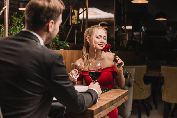 attractive woman smelling rose while sitting in restaurant with boyfriend  - Fotó, kép