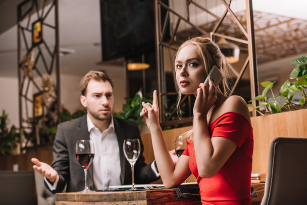 dissatisfied man looking at girlfriend talking on smartphone during dinner  - Photo, Image