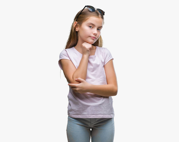 Young beautiful girl wearing sunglasses over isolated background with hand on chin thinking about question, pensive expression. Smiling with thoughtful face. Doubt concept. - Foto, imagen