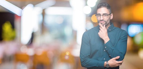 Young handsome business man wearing glasses over isolated background looking confident at the camera with smile with crossed arms and hand raised on chin. Thinking positive. - Photo, image