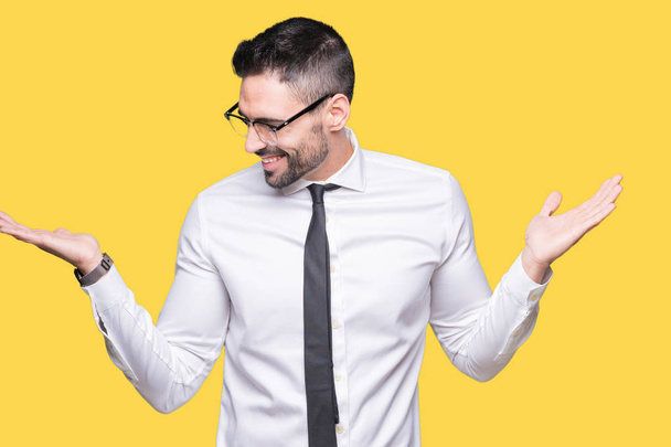 Fiatal jóképű üzletember szemüveg viselése alatt elszigetelt háttér mosolygó találat mindkét kezét meg nyitott tenyér, a bemutató, és az összehasonlító reklám és az egyensúly - Fotó, kép