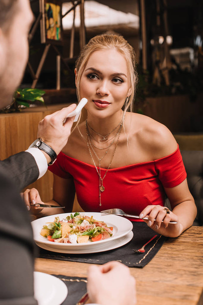 boyfriend wiping mouth of attractive blonde woman with napkin in restaurant  - Fotoğraf, Görsel