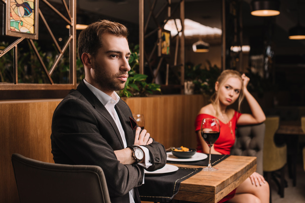 selective focus of man sitting with crossed arms near girlfriend after quarrel in restaurant  - Photo, Image