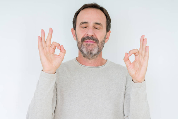 Elegante senior man over geïsoleerde achtergrond ontspannen en lachend met ogen gesloten doen meditatie gebaar met vingers. Yoga concept. - Foto, afbeelding