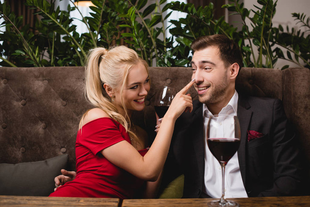 男といちゃつく、レストランでのグラスに赤ワインを押しながら鼻に触れると笑顔の女性  - 写真・画像