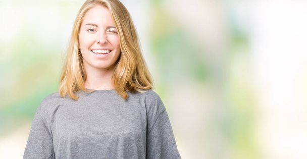 schöne junge Frau in übergroßen lässigen T-Shirt über isoliertem Hintergrund zwinkert in die Kamera mit sexy Ausdruck, fröhliches und glückliches Gesicht. - Foto, Bild