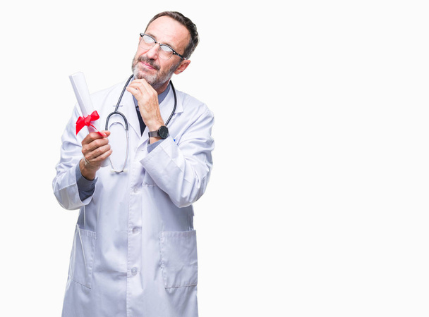 Μέση ηλικία ανώτερος γιατρός γηραιός άνδρας κρατώντας πτυχίου πάνω από το απομονωμένο φόντο σοβαρό πρόσωπο σκέψης σχετικά με την ερώτηση, πολύ συγκεχυμένη ιδέα - Φωτογραφία, εικόνα