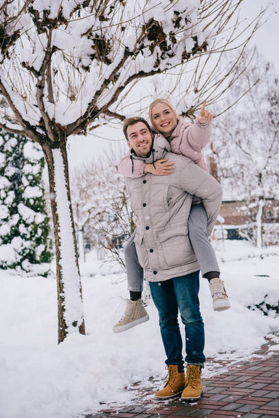 handsome man carrying playful woman pointing with finger in winter - Fotografie, Obrázek