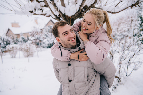 fidanzato allegro portando attraente ragazza bionda sul retro in inverno
   - Foto, immagini