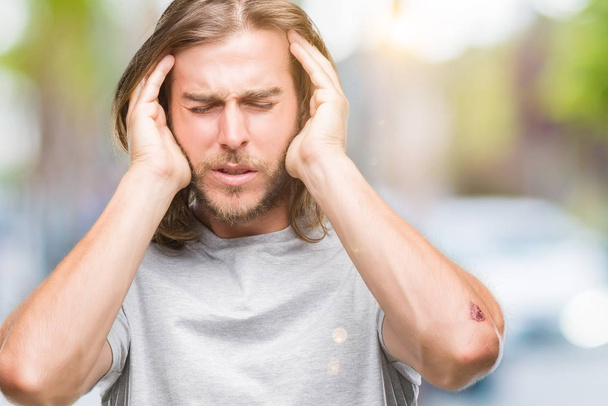 Jonge knappe man met lange haren over geïsoleerd achtergrond met hand op het hoofd voor pijn in hoofd, omdat stress. Lijden van migraine. - Foto, afbeelding
