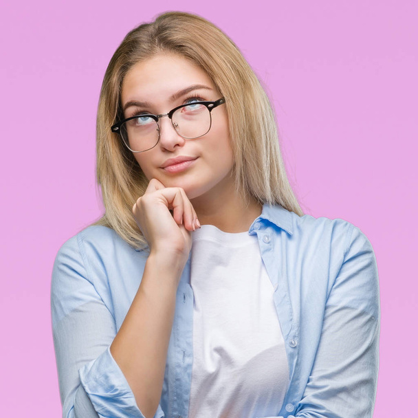 Young caucasian business woman wearing glasses over isolated background with hand on chin thinking about question, pensive expression. Smiling with thoughtful face. Doubt concept. - Photo, image