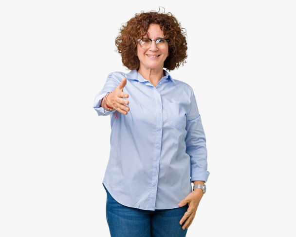 Beautiful middle ager senior businees woman wearing glasses over isolated background smiling friendly offering handshake as greeting and welcoming. Successful business. - Photo, Image