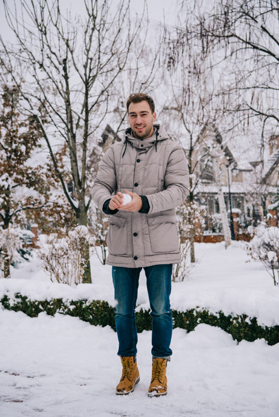 vrolijke man sneeuwbal in handen te houden in de winter  - Foto, afbeelding